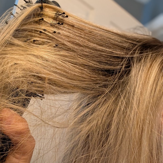 Close-up of a hand holding a hair brush with blonde hair being styled.
