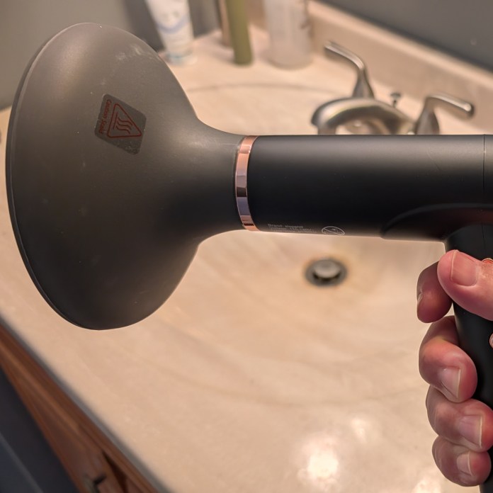 Close-up of a person's hand holding a handheld device with a large nozzle, set against a bathroom sink counter.