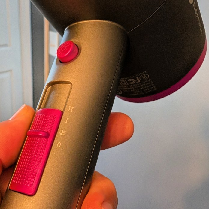 Close-up of a hand holding a hair dryer handle, featuring control buttons for speed and heat settings.