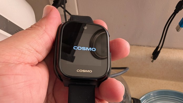 A person holding a smartwatch displaying the logo 'COSMO' on its screen.
