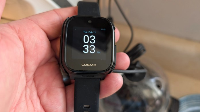 A person holding a black smartwatch displaying the time 3:33 PM and the date February 17, with the brand name 'COSMO' visible on the screen.