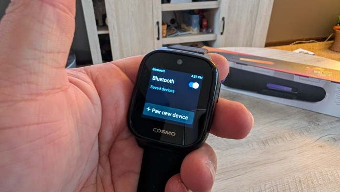 A person holding a smartwatch displaying a Bluetooth settings screen with options to pair a new device.