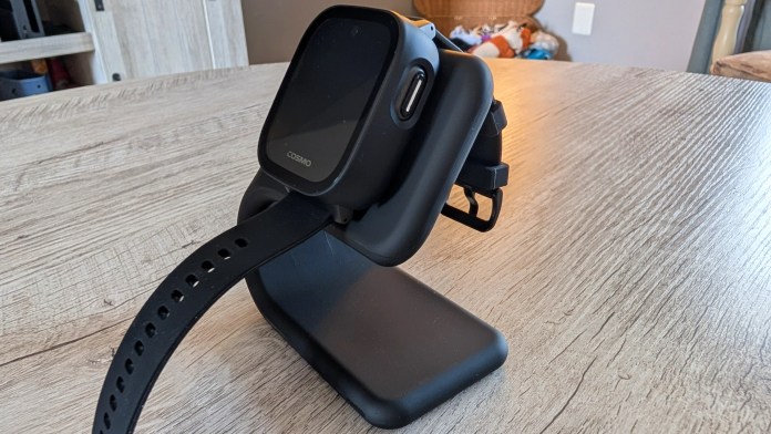 A black smartwatch charging stand with a smartwatch attached, placed on a wooden table.