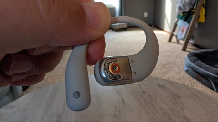 A person holding a gray wireless earbud designed for in-ear use, showcasing its sleek design and distinctive features.
