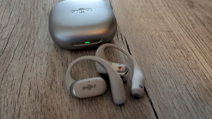 Wireless earbuds with a charging case, placed on a wooden surface.