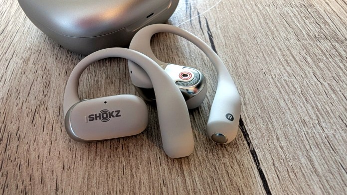 Wireless bone conduction headphones in light gray color placed on a wooden surface next to their charging case.