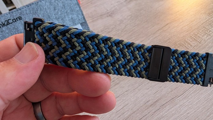 Close-up of a hand holding a woven fabric watch band with blue and green patterns against a wooden surface.