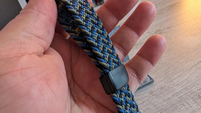 A person holding a woven strap in shades of blue and green, featuring a black clasp.