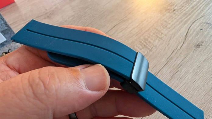 Close-up of a hand holding a flexible blue rubber strap with a metallic clasp.