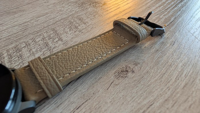 Close-up of a light brown leather watch strap on a wooden surface, showcasing its texture and clasp.