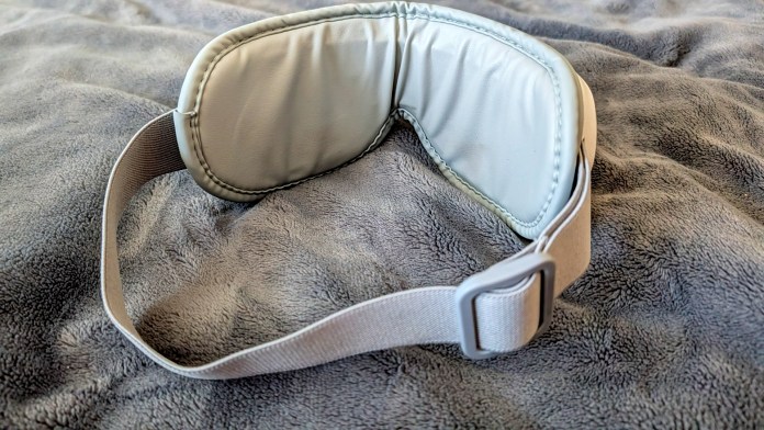A soft, padded eye mask resting on a textured gray fabric surface, designed for relaxation or sleep.