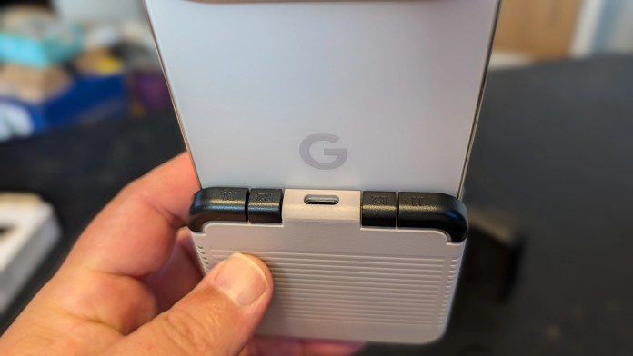 Close-up of a person holding a device with a 'G' logo, showing buttons and a charging port.