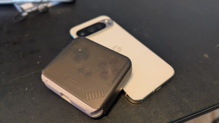 A handheld gaming controller sits on top of a smartphone placed on a dark surface.