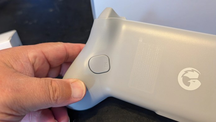 Close-up of a person's hand holding a gray gaming controller with a button labeled 'M1' on its back side.