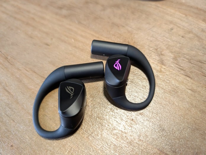 A pair of wireless earbuds with a black and pink design resting on a wooden surface.