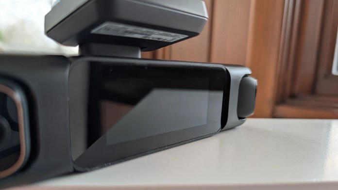 A close-up view of a modern device with a screen and a mounted component on top, placed on a surface near a window.