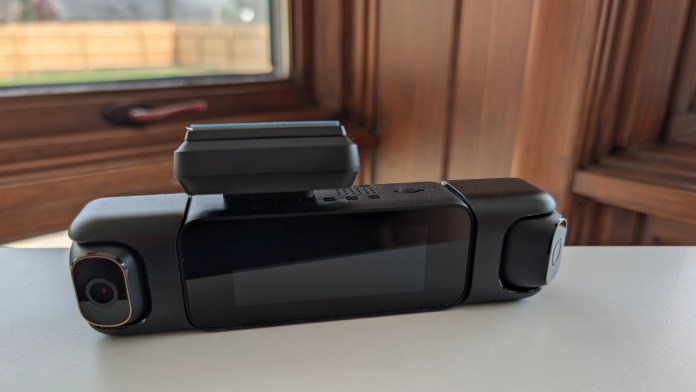 A compact camera with a screen, featuring two lenses on either side, placed on a white surface near a window.