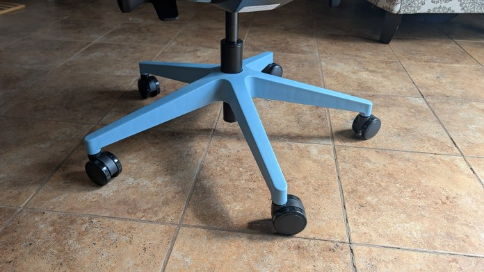 Close-up of the base of an office chair, featuring a light blue five-point star design with black rolling casters, positioned on a tiled floor.