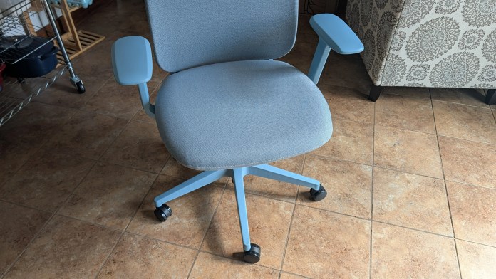 A modern gray office chair with light blue armrests and a five-point base on wheels, set on a tiled floor.