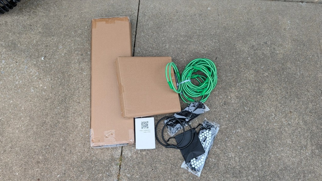 A collection of items including two cardboard boxes, a green coil of wire, and several pieces of black and white equipment packaging, placed on a concrete surface.