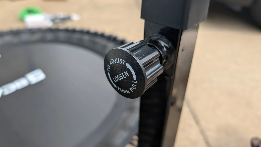 Close-up of a black adjustment knob on a trampoline, labeled 'TO ADJUST LOOSEN THEN PULL'.
