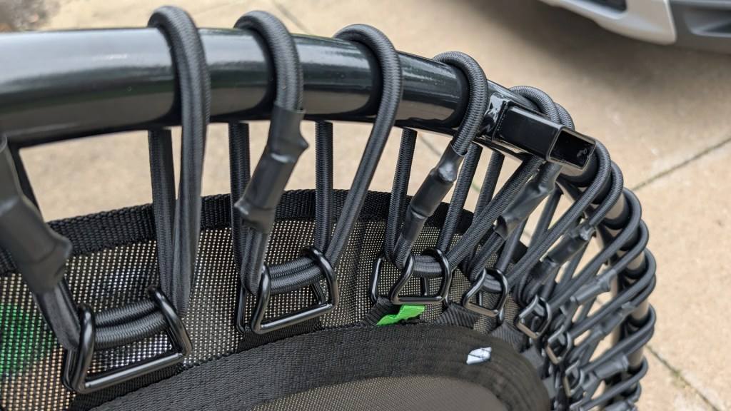 Close-up of the edge of a round trampoline with black elastic bands and hooks secured along the perimeter.