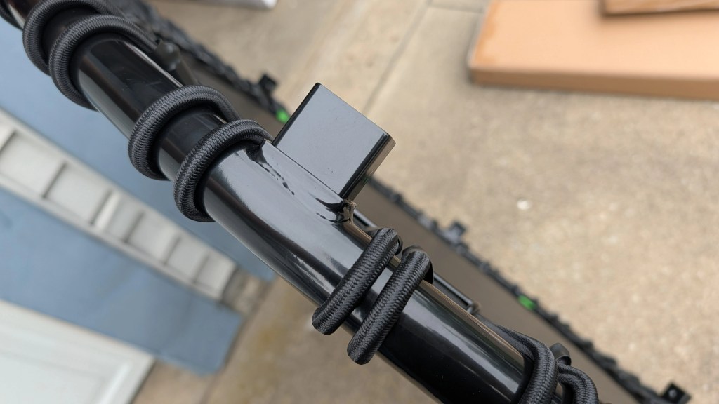 Close-up of a black pole wrapped with cord ties, featuring a small black attachment at the top.