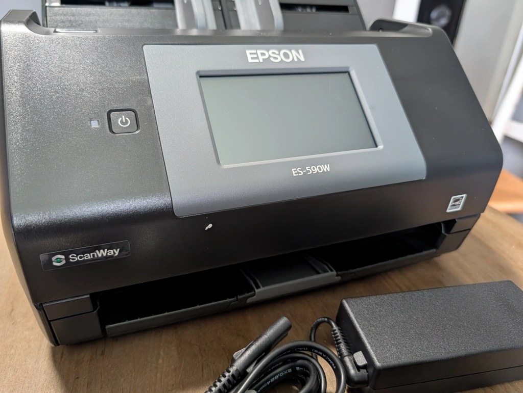 Close-up of an Epson ES-590W document scanner, featuring a control panel, power button, and connected power adapter.
