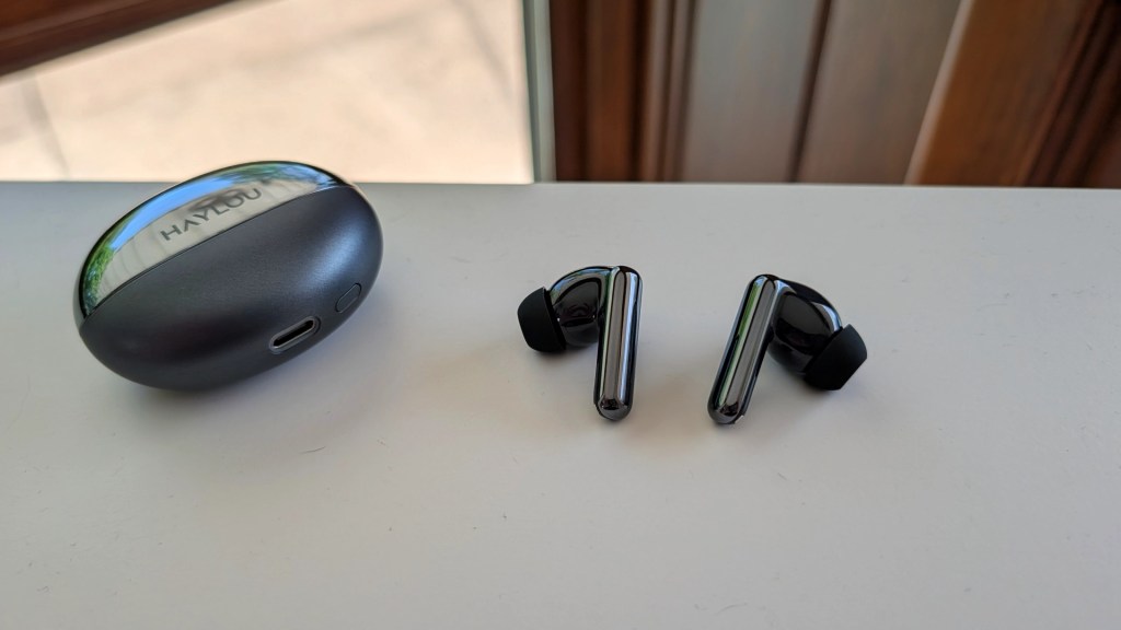 A pair of wireless earbuds next to their charging case on a white surface.