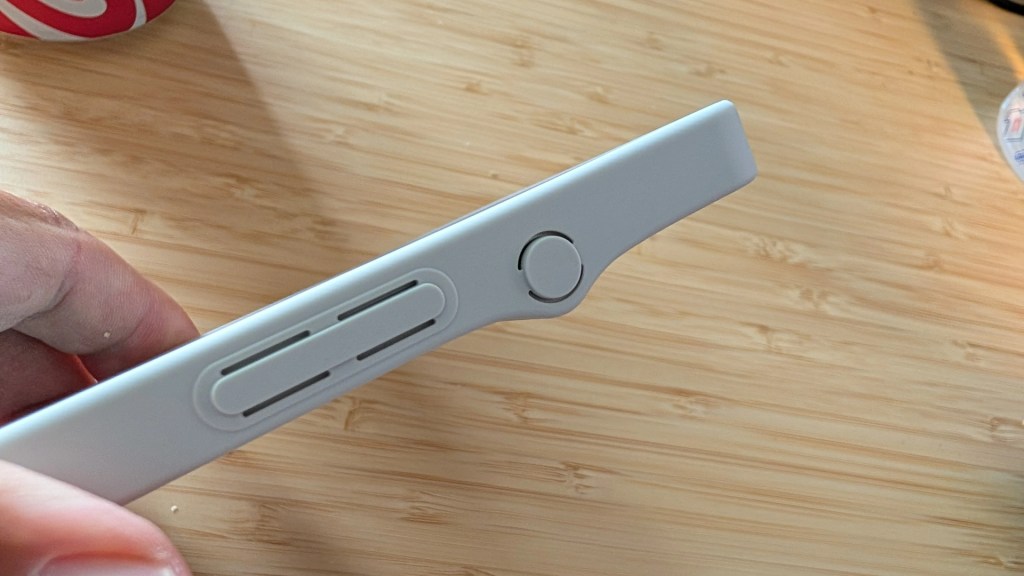 Close-up of a light gray device side showing buttons and slots, held in a hand, with a wooden surface in the background.
