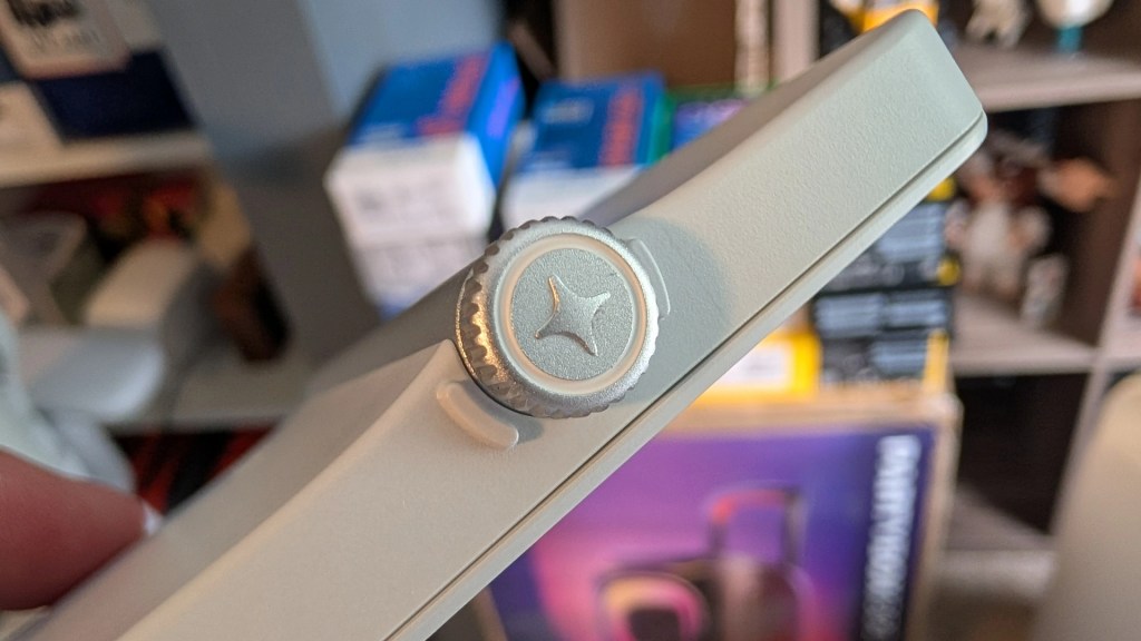 Close-up of a device side with a prominent silver dial featuring a star logo, held in a person's hand against a blurred background of boxes and shelves.