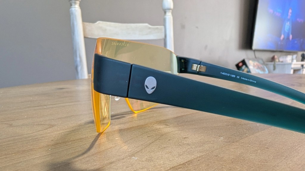A close-up of stylish sunglasses with yellow-tinted lenses and a dark frame featuring an alien logo on the side, resting on a wooden table.