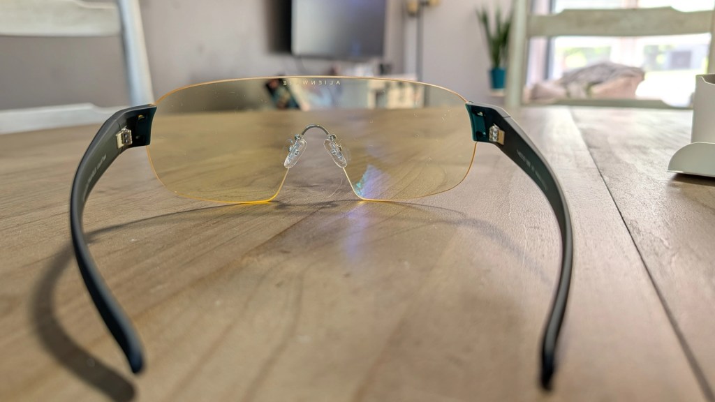 A pair of stylish sunglasses with yellow-tinted lenses, sitting on a wooden table. The frame is black with adjustable nose pads.