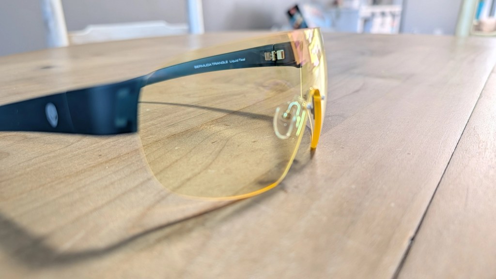Close-up of sports sunglasses with a teal frame and yellow lenses resting on a wooden surface.