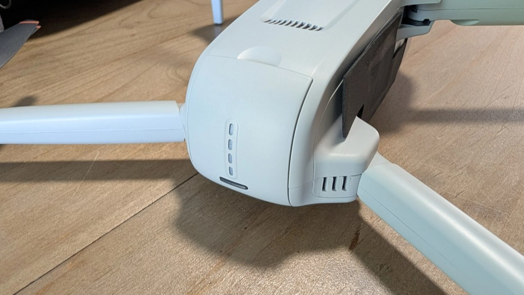 Close-up of a drone's body featuring its legs and control buttons, resting on a wooden surface.