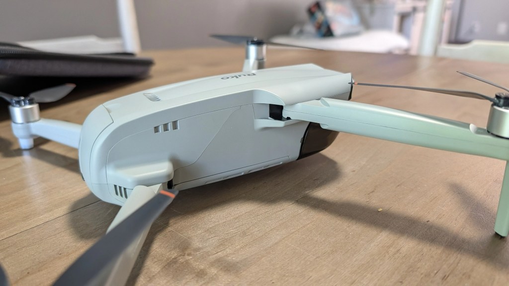 Close-up of a light-colored drone with propellers resting on a wooden table.