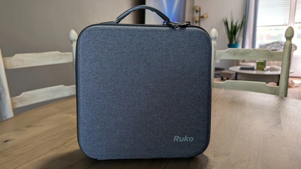 A gray fabric carrying case with a handle, displaying the brand name 'Ruko', placed on a wooden table.