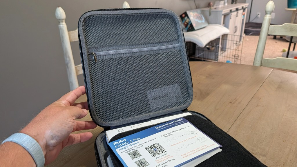 Open black zippered case with a mesh pocket and a hand holding it, displaying a quick start guide and product information inside.