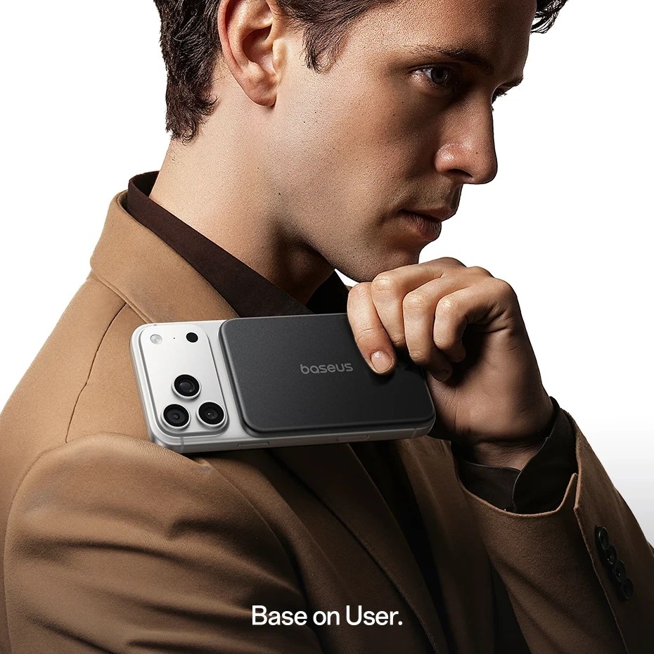 A close-up of a man in a brown blazer holding a smartphone with a black case against his shoulder, with a focus on his profile.