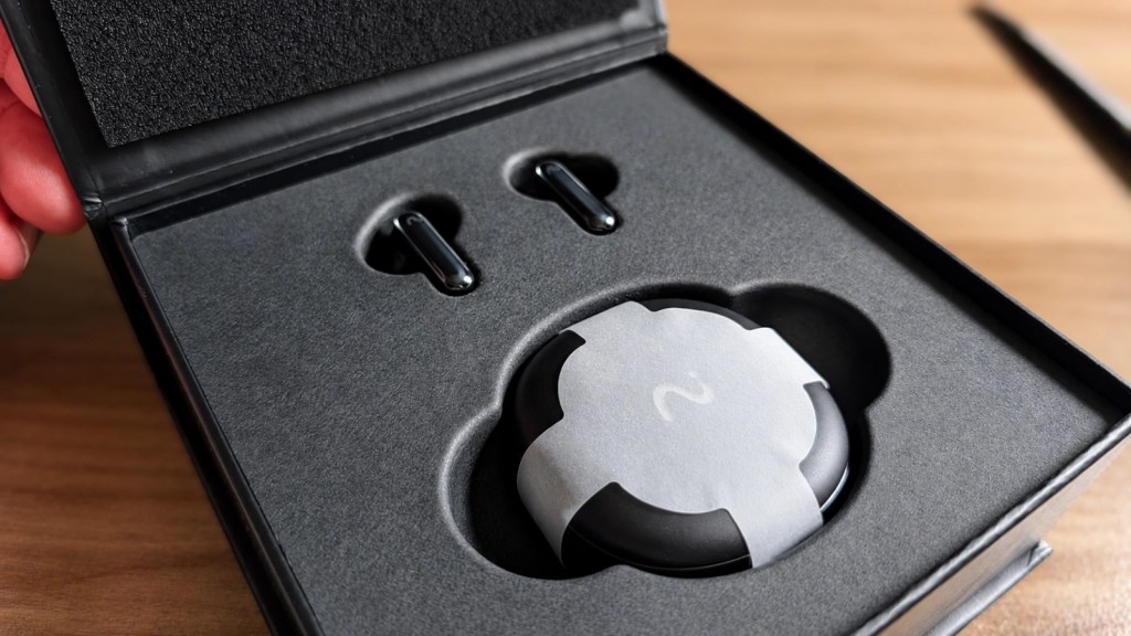 Open box containing wireless earbuds and charging case, with protective packaging.