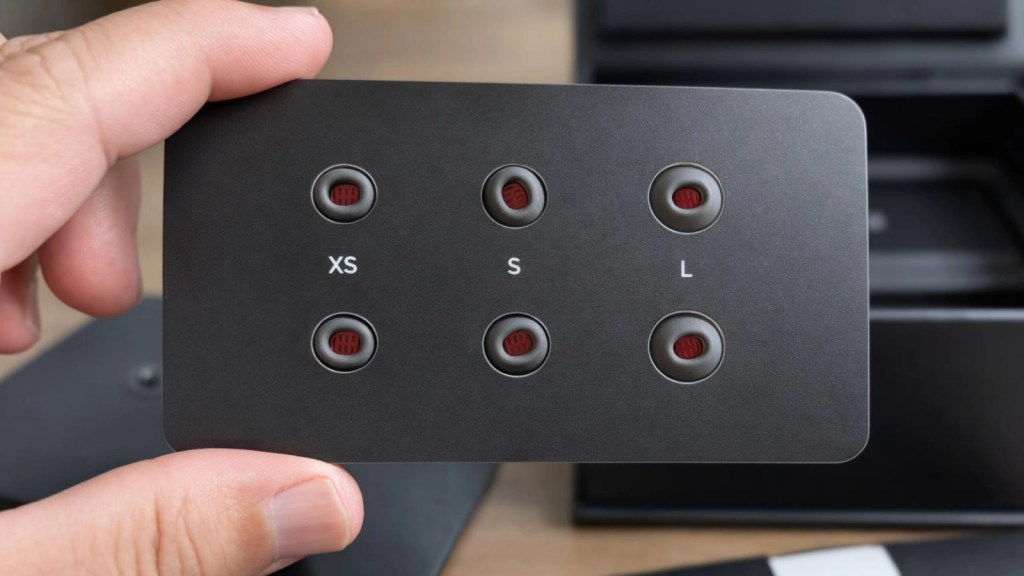 A hand holding a black rectangular card with size indicators (XS, S, L) and small circular buttons.