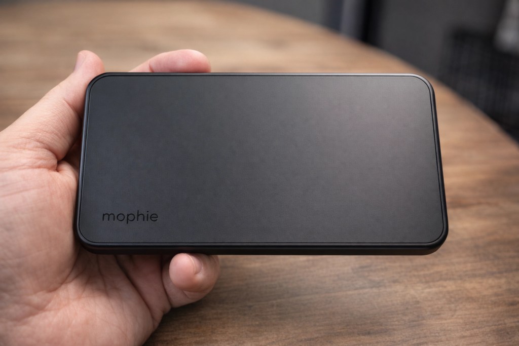 A person holding a black Mophie power bank on a wooden table.
