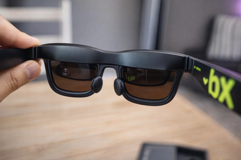 A person holding modern black sunglasses with green accents, showcasing the front view and tinted lenses.